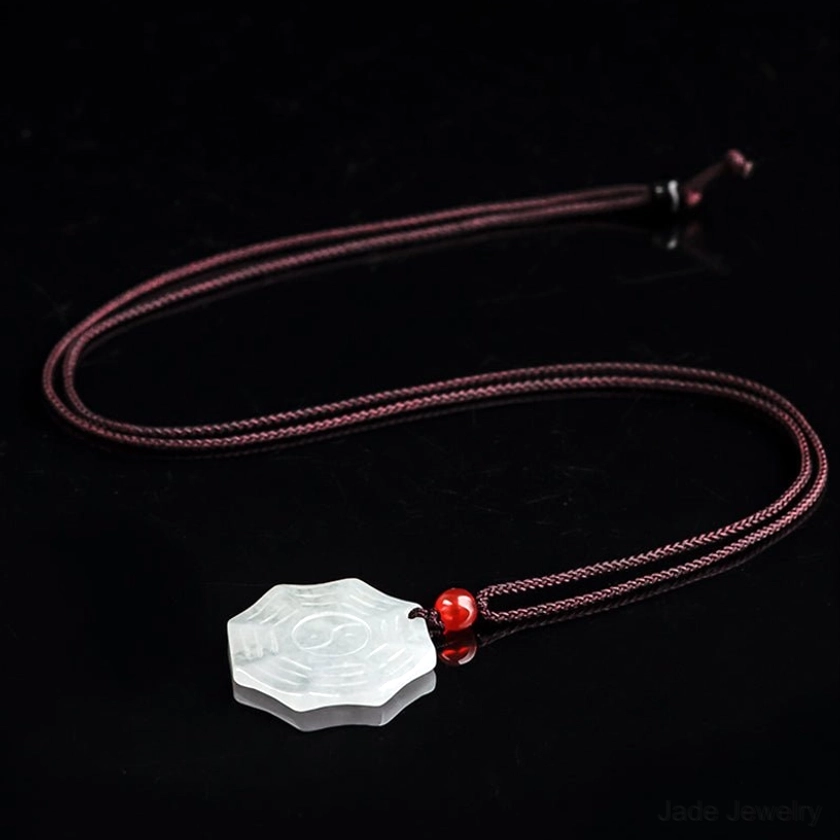 Adjustable jade Bagua Yin Yang necklace with braided brown wax cord and red agate bead slider on dark background