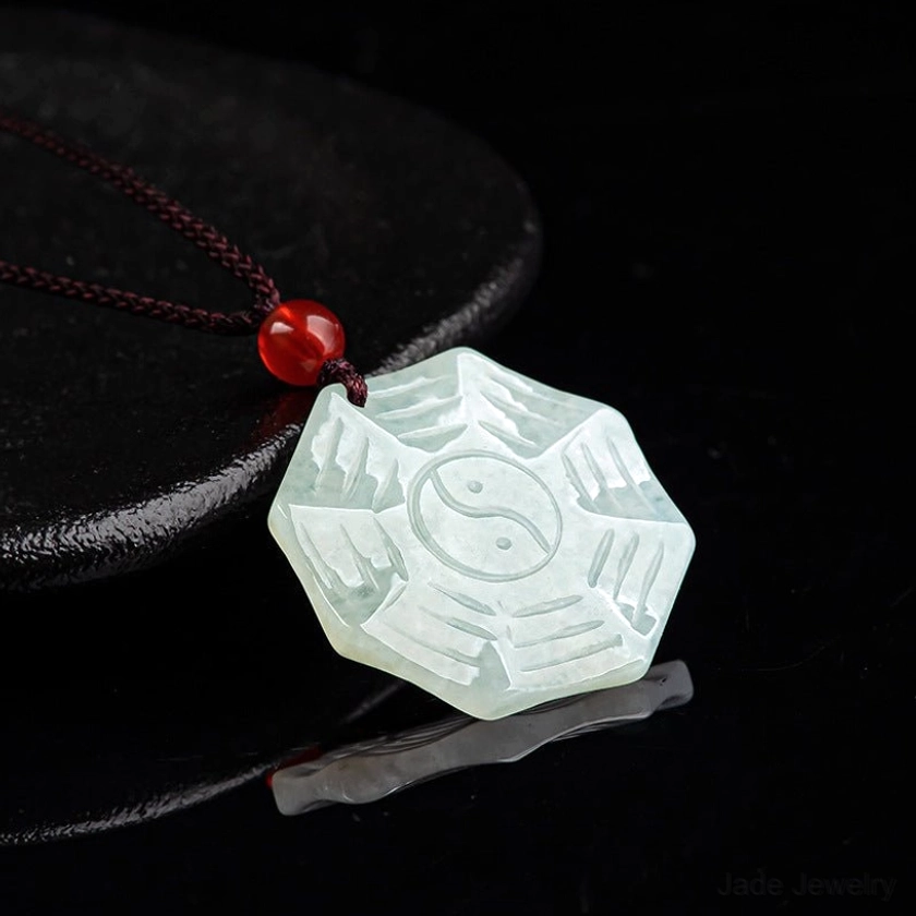 Complete natural jade Bagua Yin Yang necklace displayed on black ceramic plate with brown cord and red agate bead