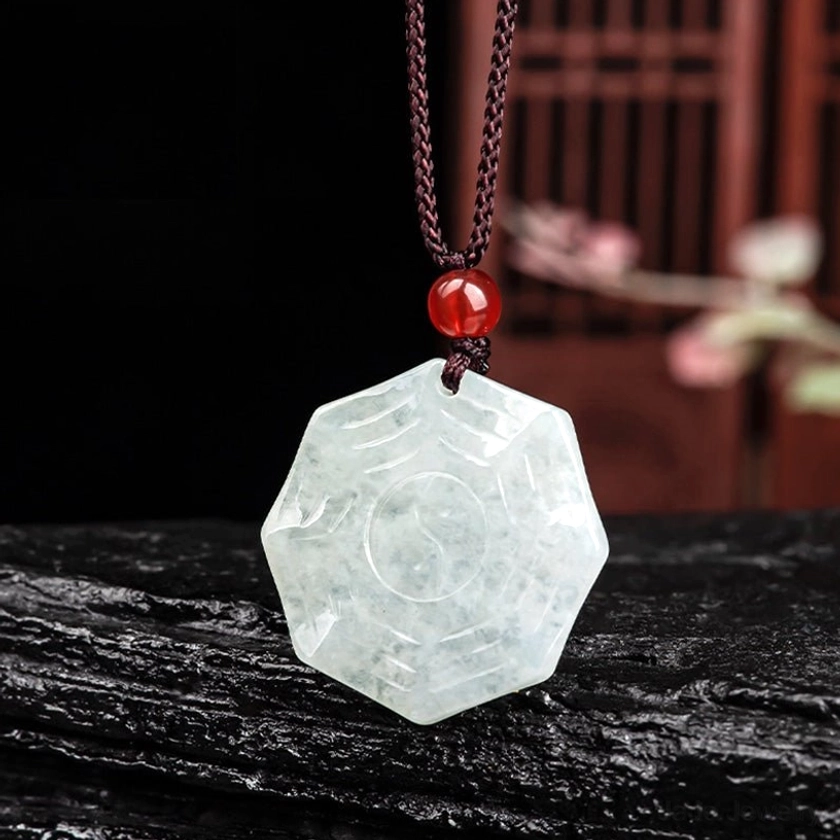 Reverse side of hand-carved jade Bagua Yin Yang pendant showing smooth tai chi symbol carving with red agate bead accent