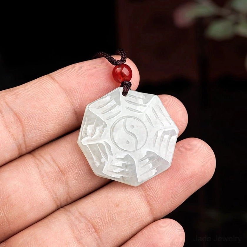 Hand-held jade Bagua Yin Yang pendant showing detailed trigram and tai chi carving with brown wax cord adjustment