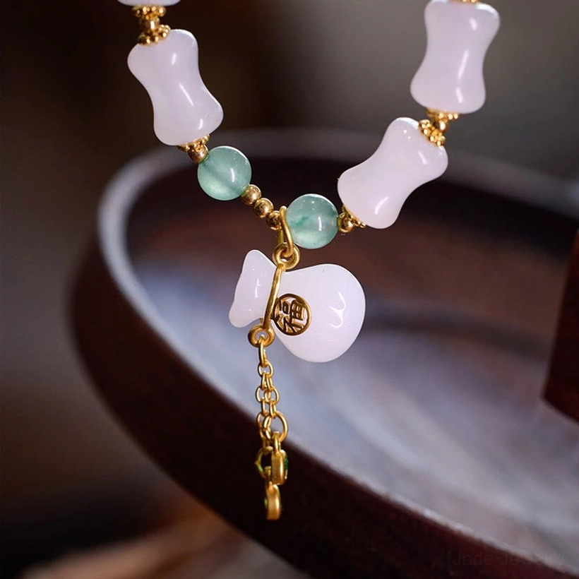 Close-up detail of milky white bamboo-carved jade beads and gold tassel pendant hardware on jade prosperity bracelet