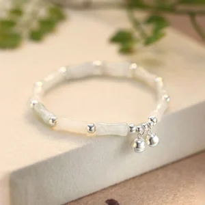 Hetian white jade bamboo bell bracelet featuring polished silver hardware and smooth off-white jade segments - three-quarter view with green plants