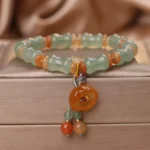 Natural jade bamboo beaded bracelet with orange agate flower charm displayed on white satin jewelry box