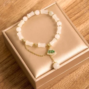 Close-up top view of jade bamboo bracelet beads with delicate carvings, gold chain accents, and green enamel fan charm on wooden display tray