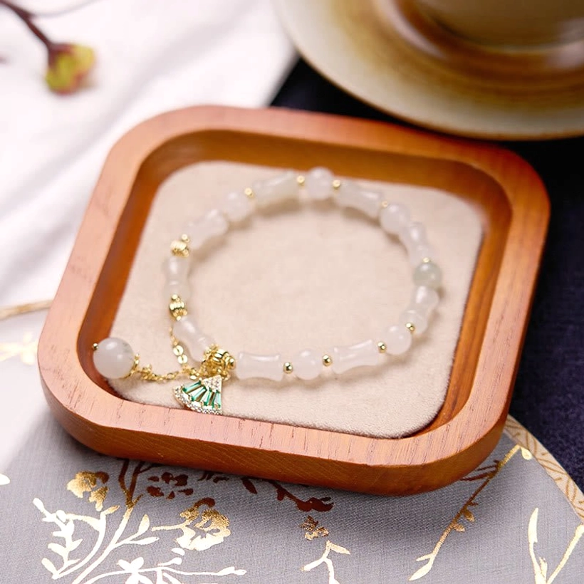 Detailed overhead view of white jade bamboo pattern beads and green charm on embroidered fabric, highlighting natural stone texture and handcrafted quality
