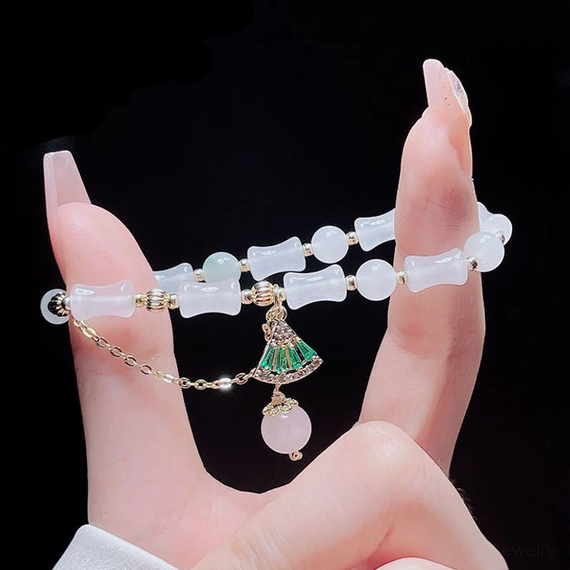 Delicate close-up of white jade bamboo and round beads on fingertips, displaying individual bead craftsmanship and the decorative green charm