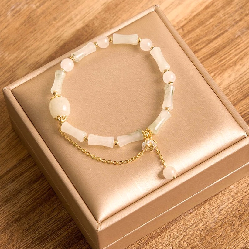 Flat lay overhead view of authentic Tianshan white jade bamboo bracelet with pale yellowish-white beads, gold metal hardware, and dangling pearl pendant