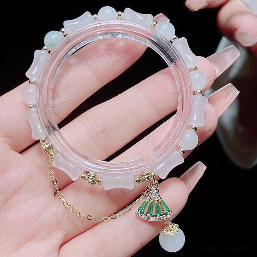 Hand holding Tianshan white jade bamboo bracelet showing frosted finish beads, gold chain, and green fan charm with round jade drop