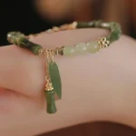 Green jade bamboo leaf prosperity bracelet worn on wrist, showing natural green beads with gold-tone bamboo charm pendant