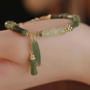 Green jade bamboo leaf prosperity bracelet worn on wrist, showing natural green beads with gold-tone bamboo charm pendant