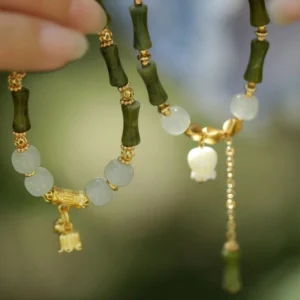 Two matching green jade bamboo bracelets with lily charm and pearl tassel, overhead close-up view