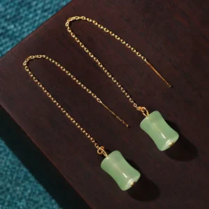 Light green jade bamboo earrings pair displayed on wooden table with blue fabric, side angle showcase