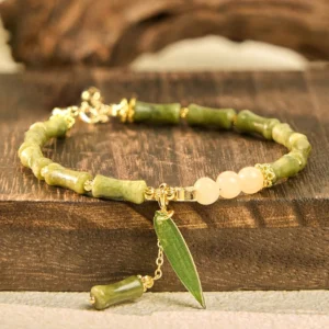 Flat lay display of jade bamboo bracelet on wooden surface, featuring mixed green jade and pale beads with dangling leaf charm
