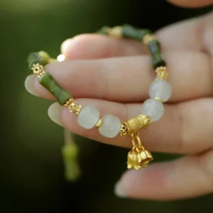 Green jade bamboo bracelet with lily of the valley gold charm held in hand, outdoor natural lighting