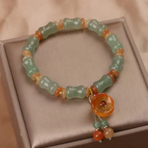 Green carved jade beads with bamboo pattern and orange spacer beads featuring agate flower pendant on brown display tray