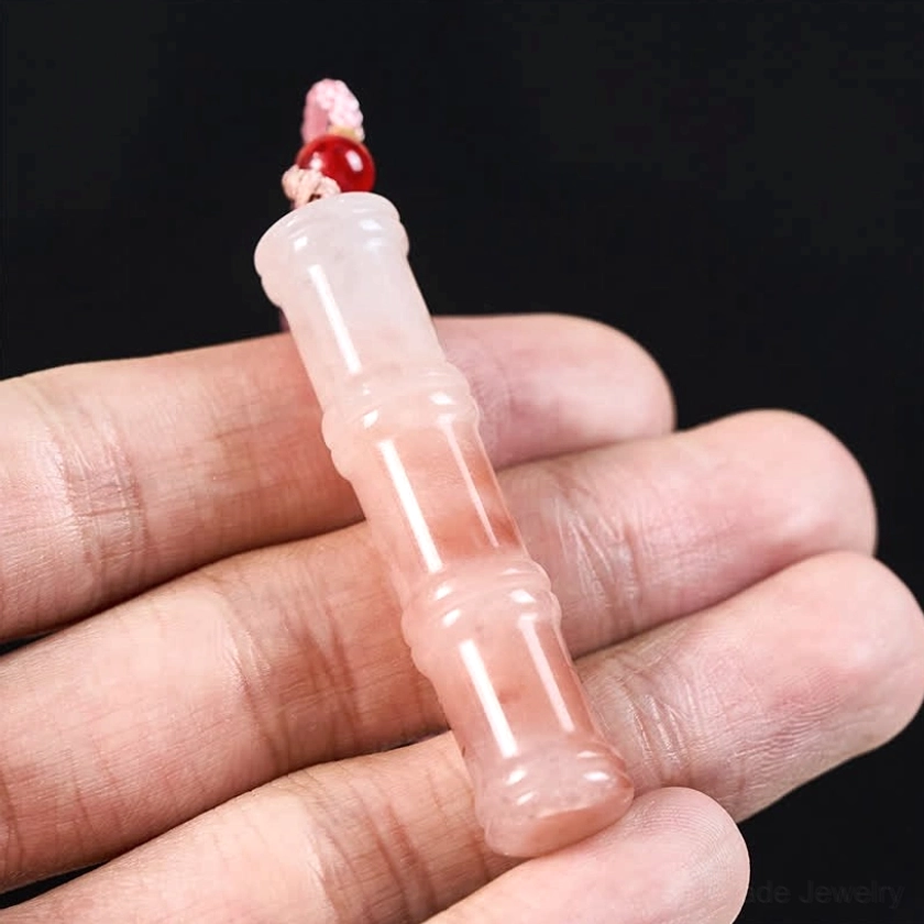 Close-up hand-held view of pink quartzite jade bamboo pendant showing intricate carved bamboo joint details, translucent stone quality, and handmade craftsmanship
