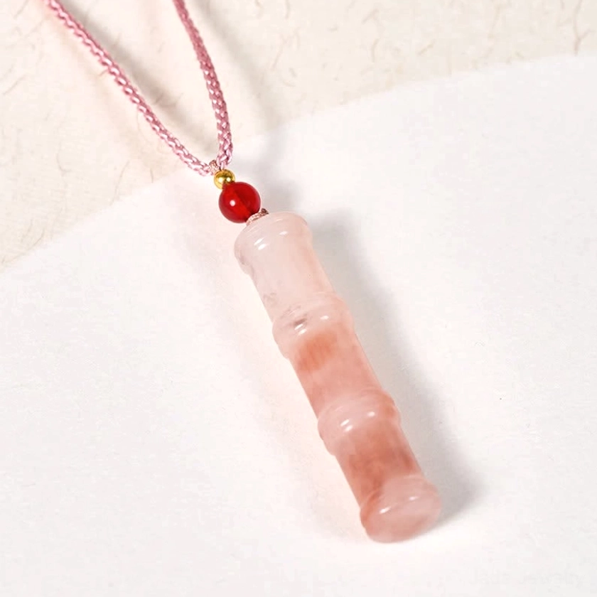 Side profile of pink quartzite jade bamboo pendant necklace suspended on fabric background, displaying pendant shape, braided cord, and translucent stone quality