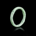 Natural green jade bamboo ring with carved joint details displayed at oblique angle on black background, showing polished finish and natural stone veining
