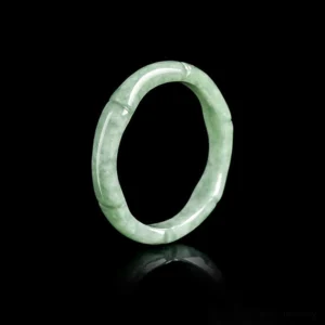 Natural green jade bamboo ring with carved joint details displayed at oblique angle on black background, showing polished finish and natural stone veining