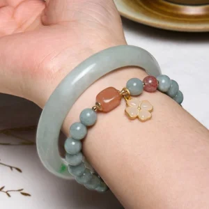 Stacked jade bangle and beaded bracelet on wrist showcasing fit and design with decorative charms