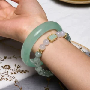 Jade bangle and beaded bracelet set worn on wrist with embroidered tabletop background showing side profile