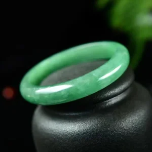 Bright green jade bangle bracelet displayed at angle, highlighting polished surface and vibrant jade color under natural lighting