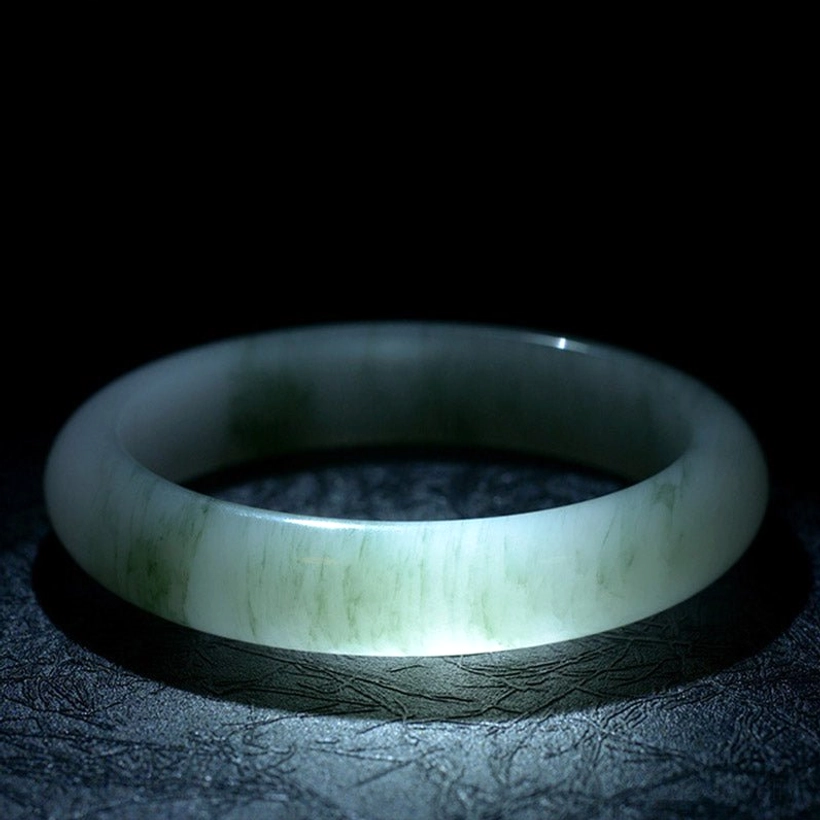Pale green jade bangle bracelet overhead backlit view highlighting natural internal patterns and light translucency