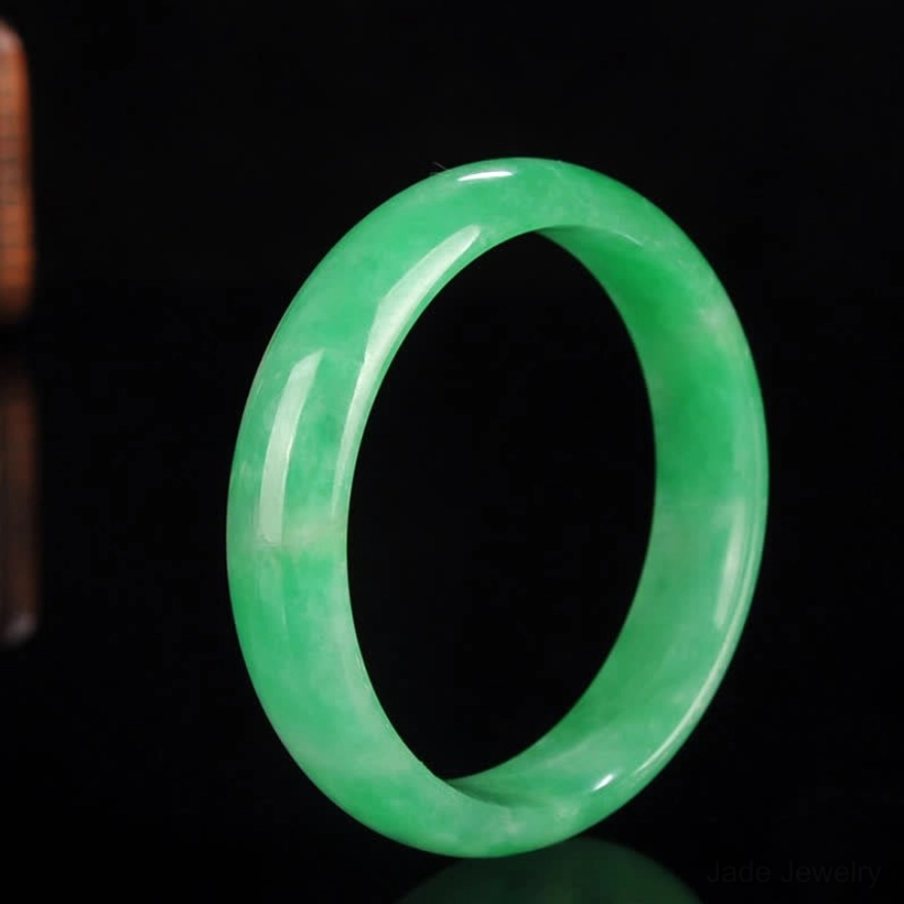 Even emerald green jade bangle bracelet in minimalist design, centered front view against black background
