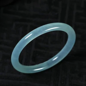 Natural jade bangle bracelet flat lay view showcasing even light blue hue and perfectly polished round band on dark background