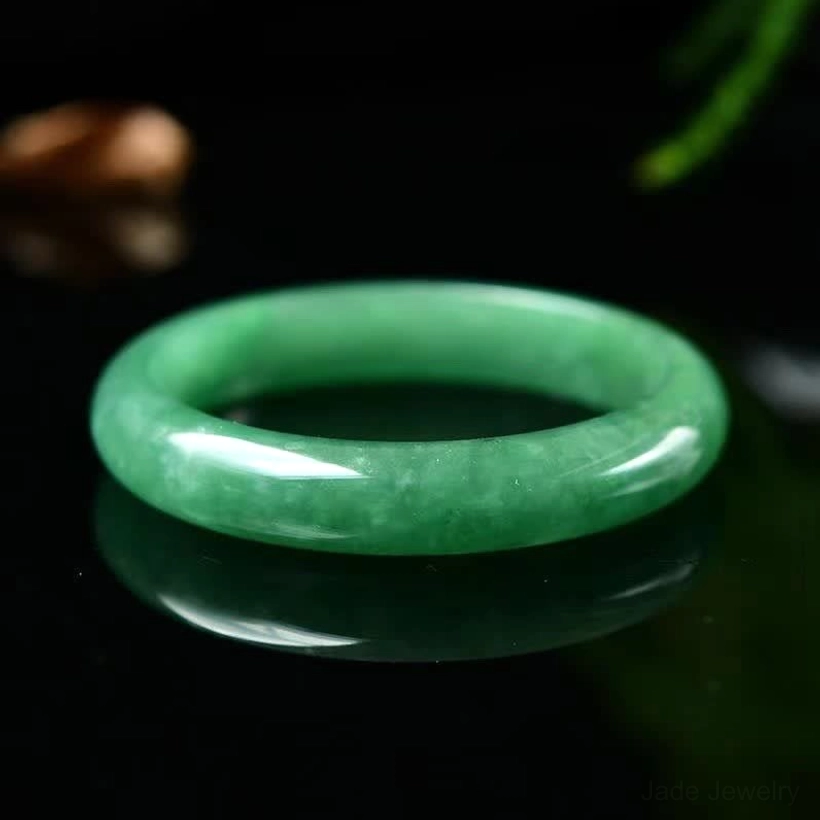 Deep forest green natural jade bangle placed on reflective black surface, showing smooth polished finish from overhead
