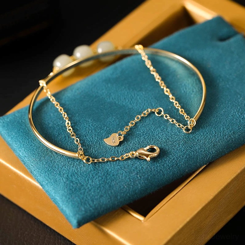 Top down view of jade bangle bracelet with four light green beads and heart shaped chain charm on blue velvet display
