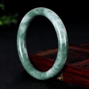 Natural green and white marbled jade bangle bracelet displayed on wooden jewelry base, front view showing prosperity stone