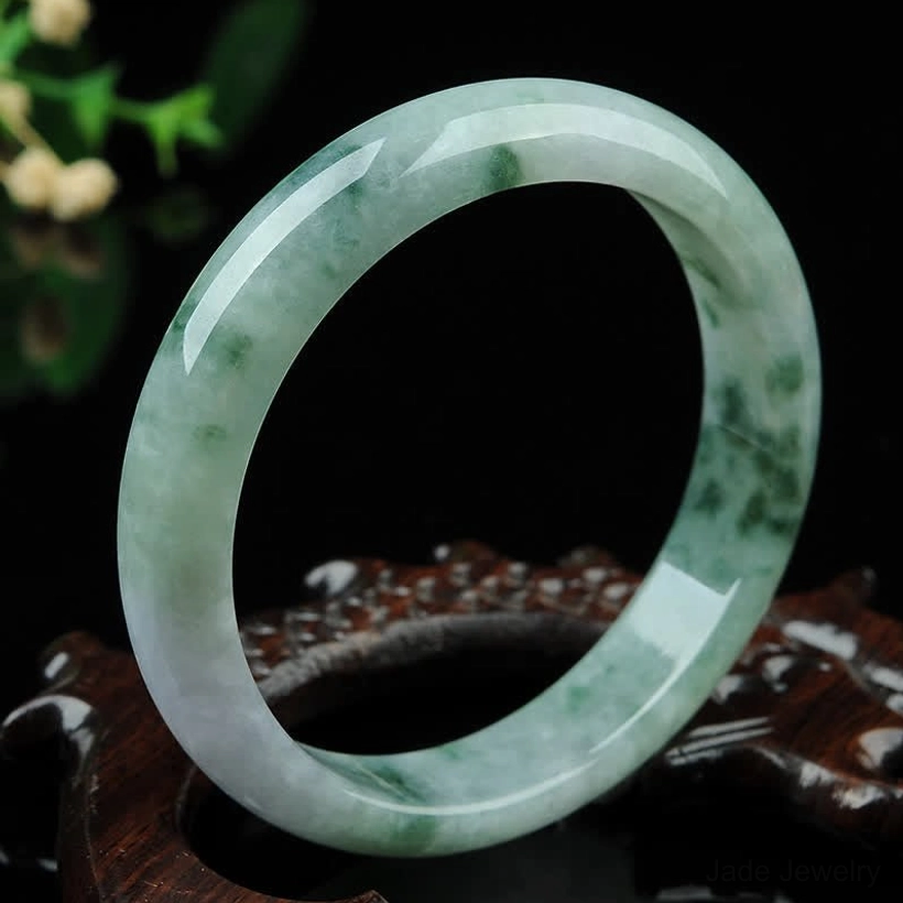 Natural jade bangle bracelet with dark green spotted texture, smooth polished finish, overhead view on wooden prop