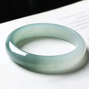 Translucent jade bangle bracelet in aqua to light green gradient tone viewed from above on white background, showcasing smooth polished surface and uniform inner diameter