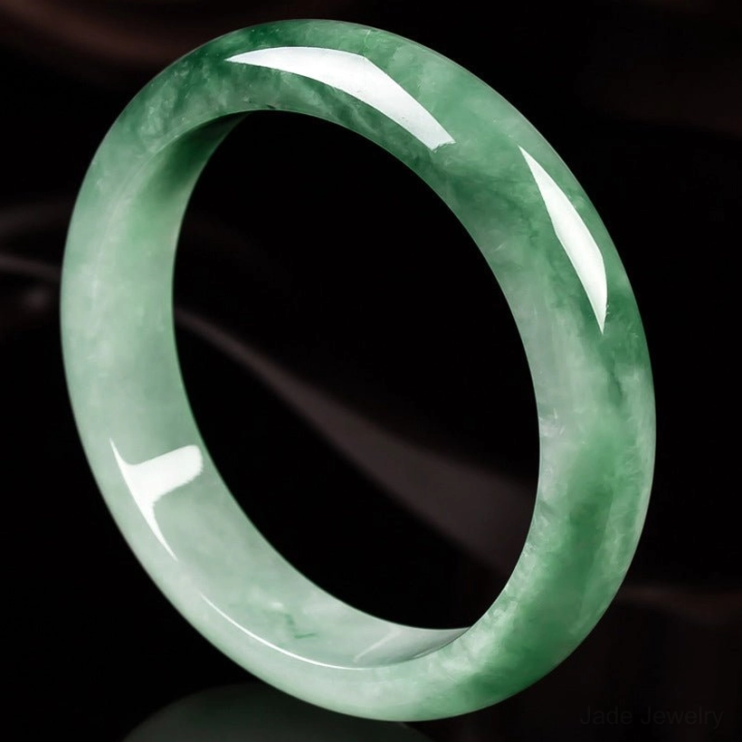 Rounded natural jade bangle bracelet with unique green patterns, glossy polished edge, side view