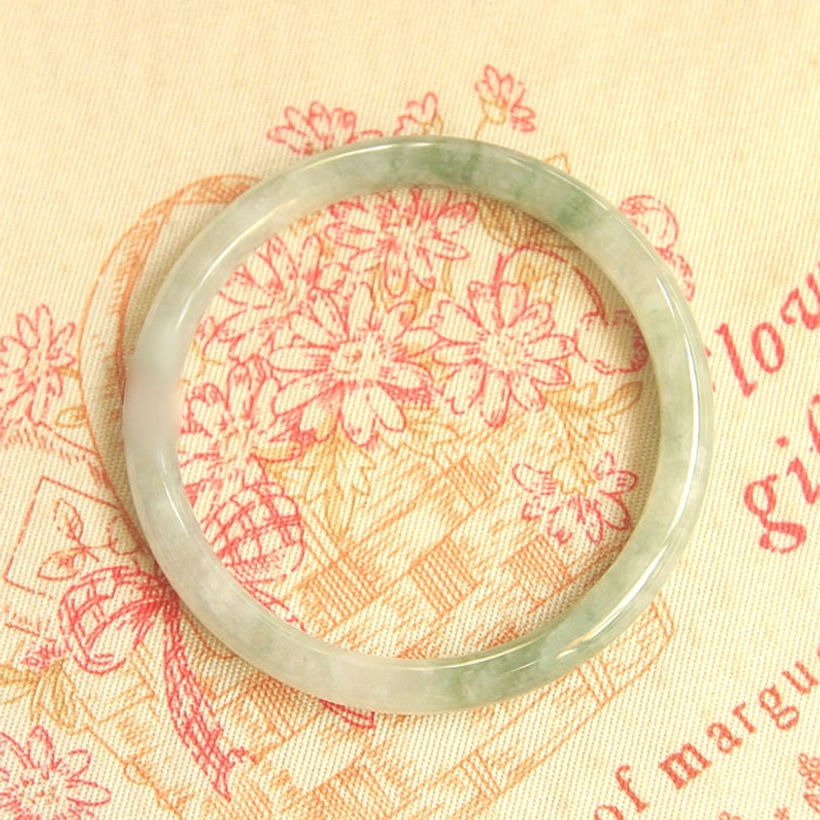 Polished natural jade bangle bracelet showing green vein textures from direct overhead view on decorative fabric