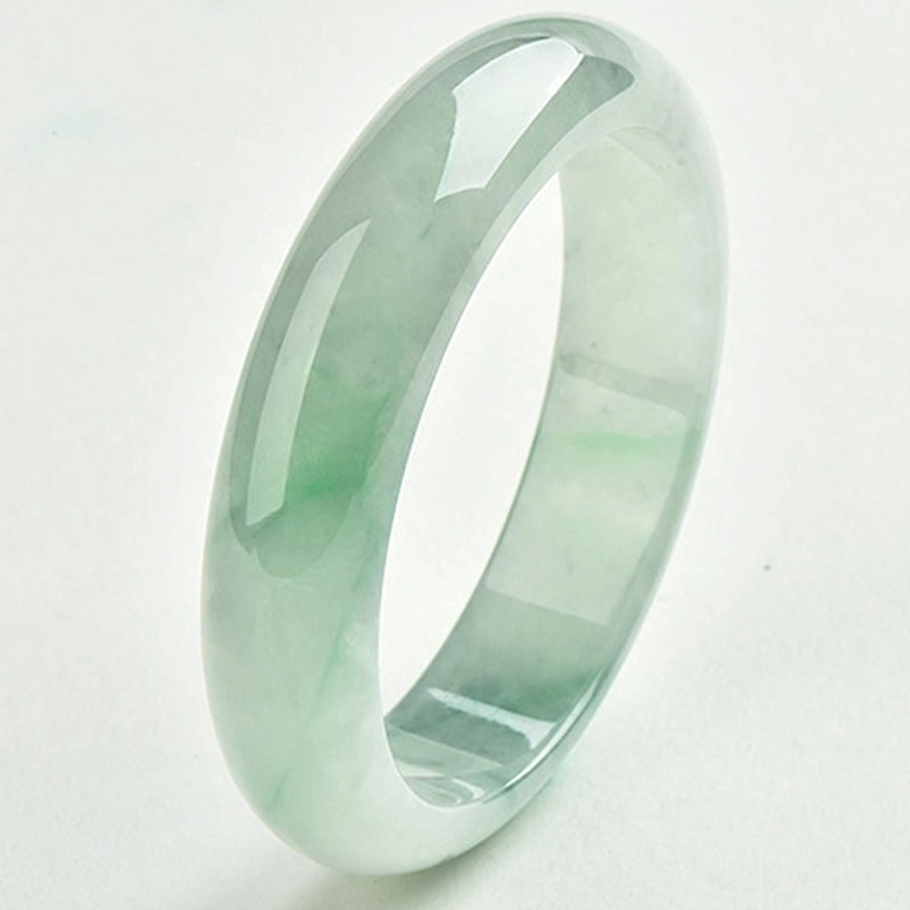 Smooth polished jade bangle bracelet in pale green with faint streaks, side three-quarter view on off-white background demonstrating fine craftsmanship and high-gloss finish