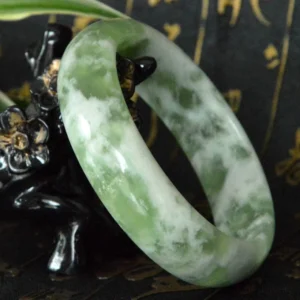 Authentic jade bangle bracelet showing mixed green white stone veins, oblique side angle with decorative background