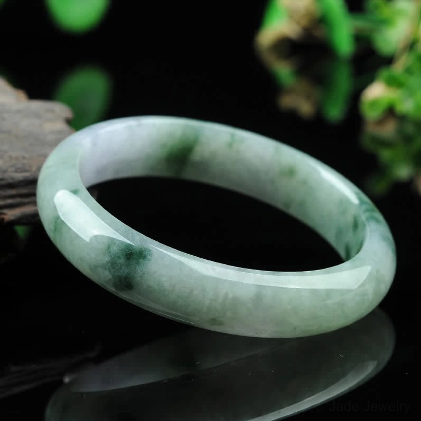 Jade bangle bracelet low angle view showing round smooth band with light green base and natural dark flecks