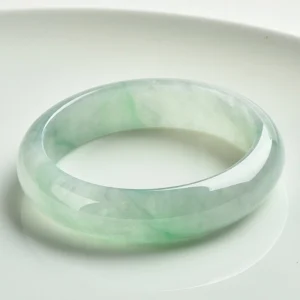 Natural jade bangle bracelet with light green translucent finish, displayed on white ceramic plate showing polished smooth jade surface and natural color variations