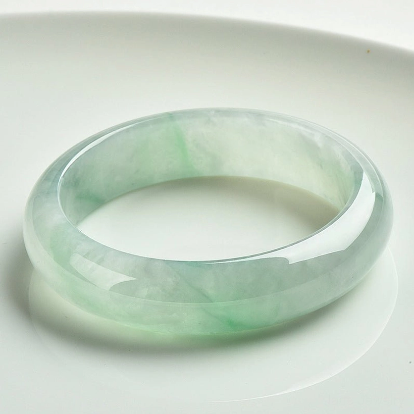 Natural jade bangle bracelet with light green translucent finish, displayed on white ceramic plate showing polished smooth jade surface and natural color variations