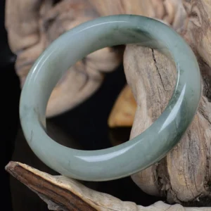 Celadon jade bangle bracelet with dark green streaks, top-down side view showing thick rounded band
