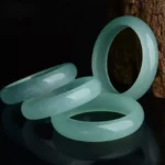 Multiple natural jade bangle bracelets stacked in light cyan and green colors displayed on dark reflective surface