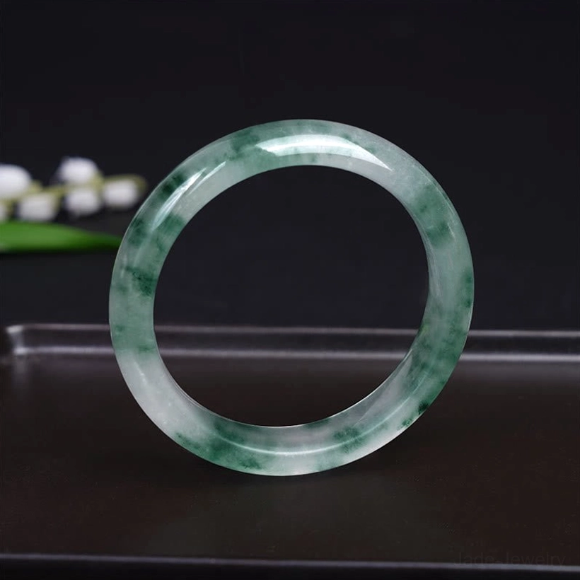Polished jade bangle front flat view showcasing glossy finish and distinct green floating flower pattern