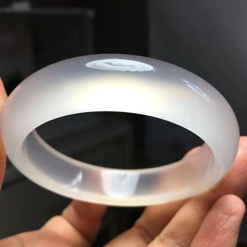 Single jade bangle held in hand close-up view showing smooth rounded edges and translucent white finish