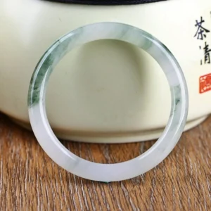 Lavender and green jade bangle bracelet displayed on wooden table with ceramic jar
