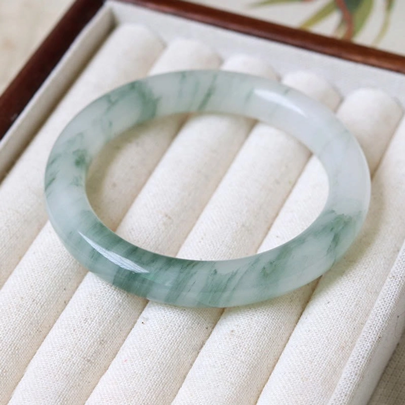 Natural jade bangle bracelet placed on luxury velvet jewelry display cushion, flat lay showing polished surface and green veined finish
