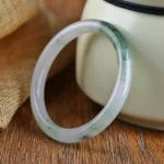 Natural jade bangle bracelet with white base and dark green floating patterns on wooden surface