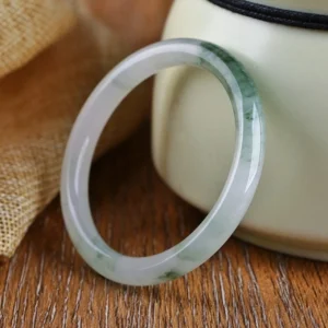 Natural jade bangle bracelet with white base and dark green floating patterns on wooden surface