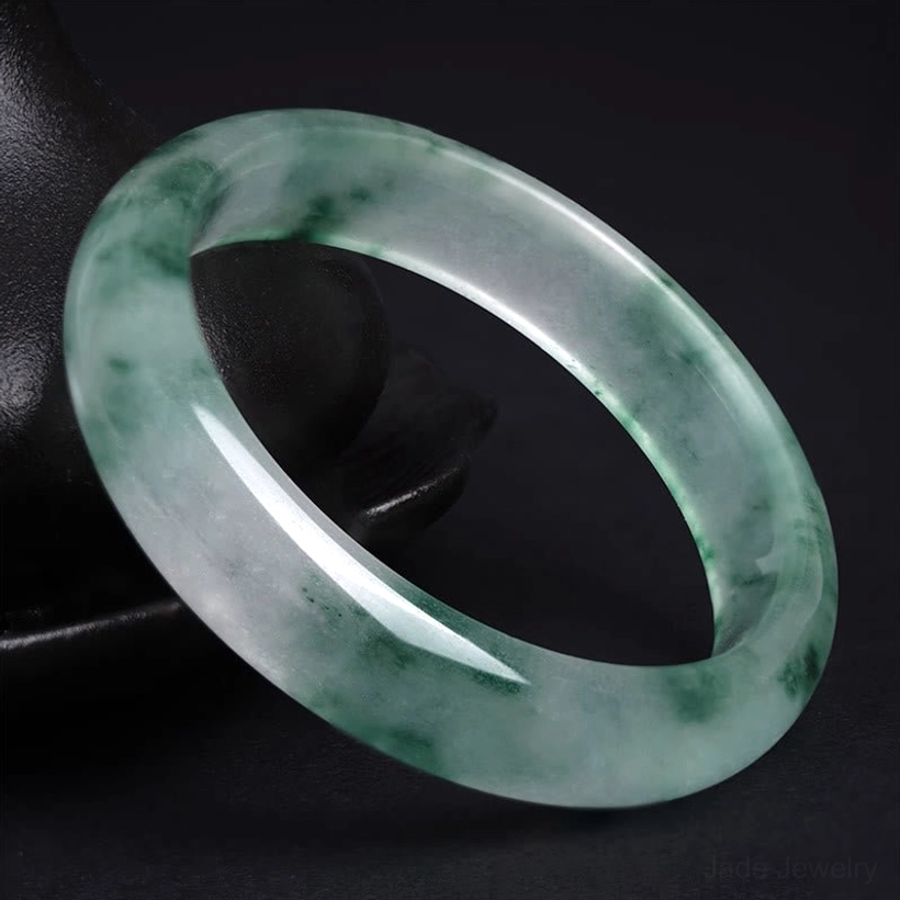 Low-angle side view of natural jade bangle showing smooth polished edge and translucent base with dark green veins